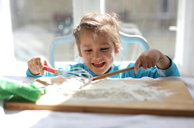 Smiling girl playing with flour and kitchen tools indoors. Captures innocence and fun.