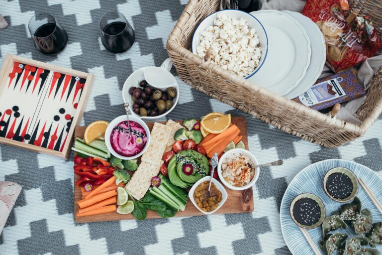 Colorful vegan picnic setup with variety of vegetables and snacks on a patterned blanket.